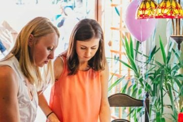 Two women standing around a table of fruit and sweets, Natasha is cutting a cake