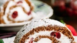 A slice of chocolate cherry roll with rum cream with the whole roll in the background