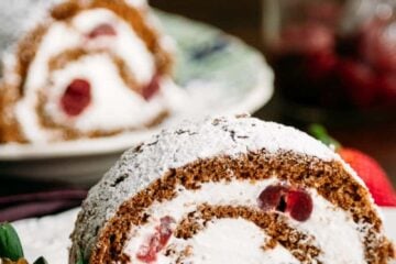 A slice of chocolate cherry roll with rum cream with the whole roll in the background