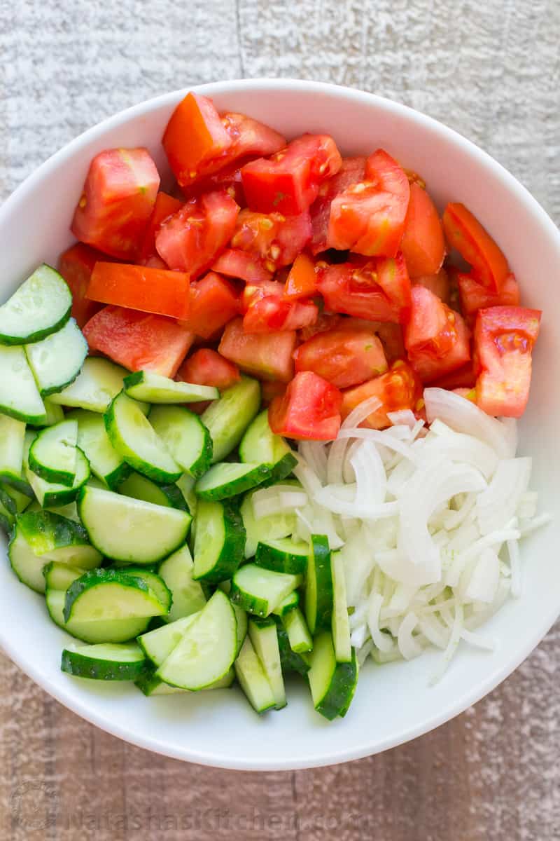Salad bowl filled with Ingredients for cucumber tomato onion salad including fresh chopped tomatoes, sliced cucumbers and sliced onions.