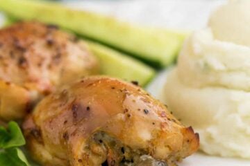 A plate of baked mushroom stuffed chicken thighs besides mashed potatoes and cucumbers