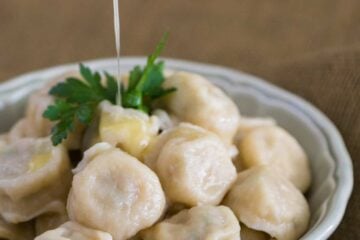 A white bowl of Russian chicken pelmeni with butter being poured over the top of them