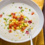 Creamy cauliflower soup in a bowl with a spoon, garnished with bacon, parsley and corn
