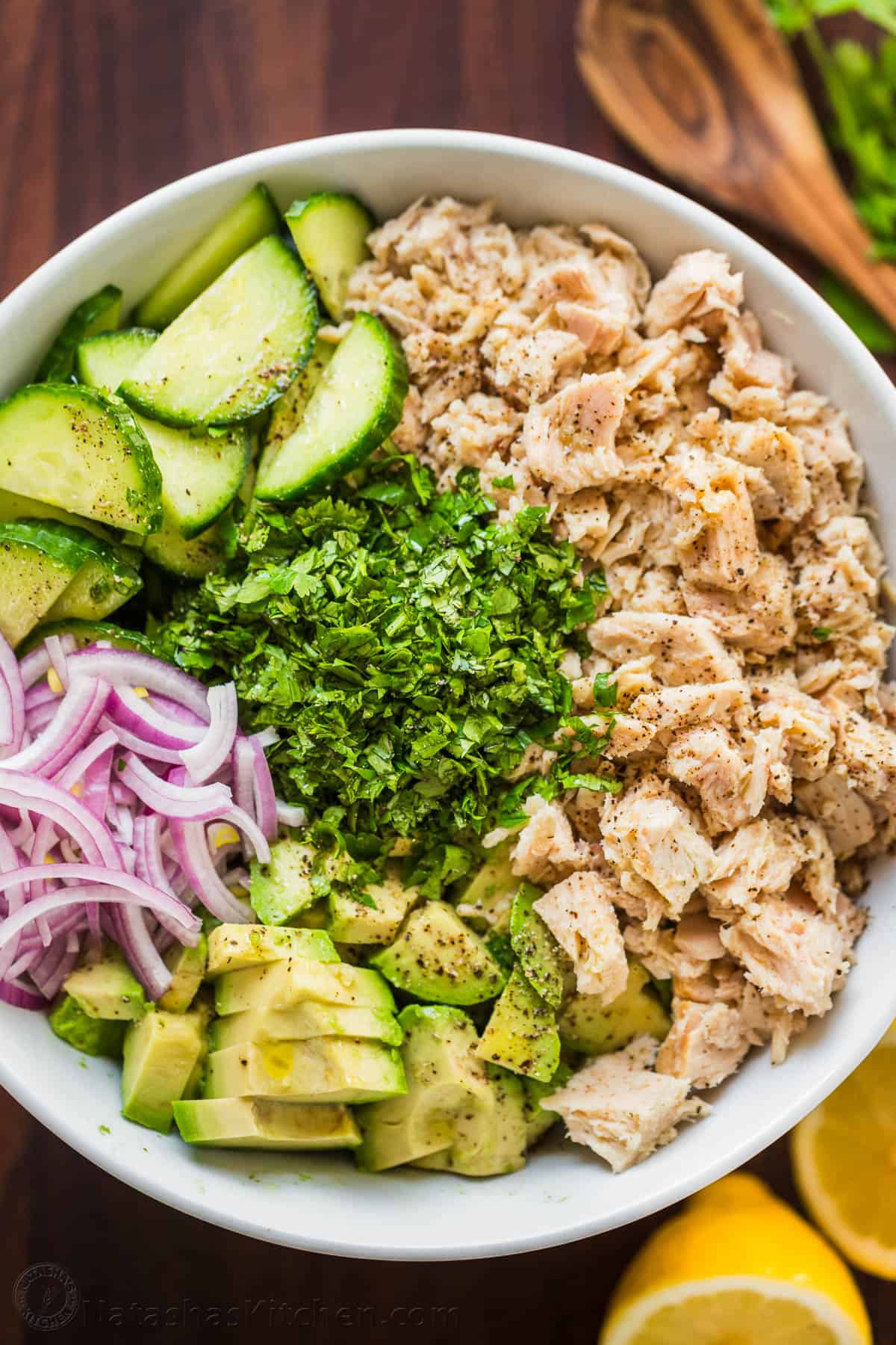 This Avocado Tuna Salad has incredible fresh flavor. It' is a high-protein salad and the avocado adds creaminess without any mayo. Ingredients added in sections to a serving bowl with tuna, avocado, red onion, cucumber and cilantro.