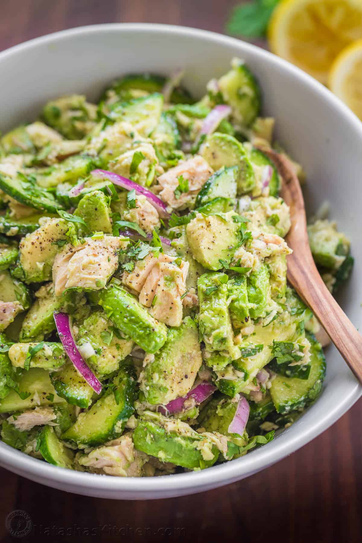 This Avocado Tuna Salad has incredible fresh flavor. It' is a high-protein salad and the avocado adds creaminess without any mayo. Avocado tuna salad served in a white bowl with a serving spoon.