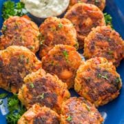 A blue plate with Salmon cakes garnished with parsley and a small bowl of tartar sauce