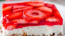 A slice of Strawberry Pretzel Salad on a white plate with the whole dessert in the background