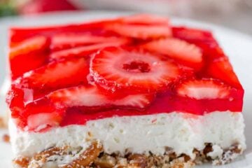 A slice of Strawberry Pretzel Salad on a white plate with the whole dessert in the background