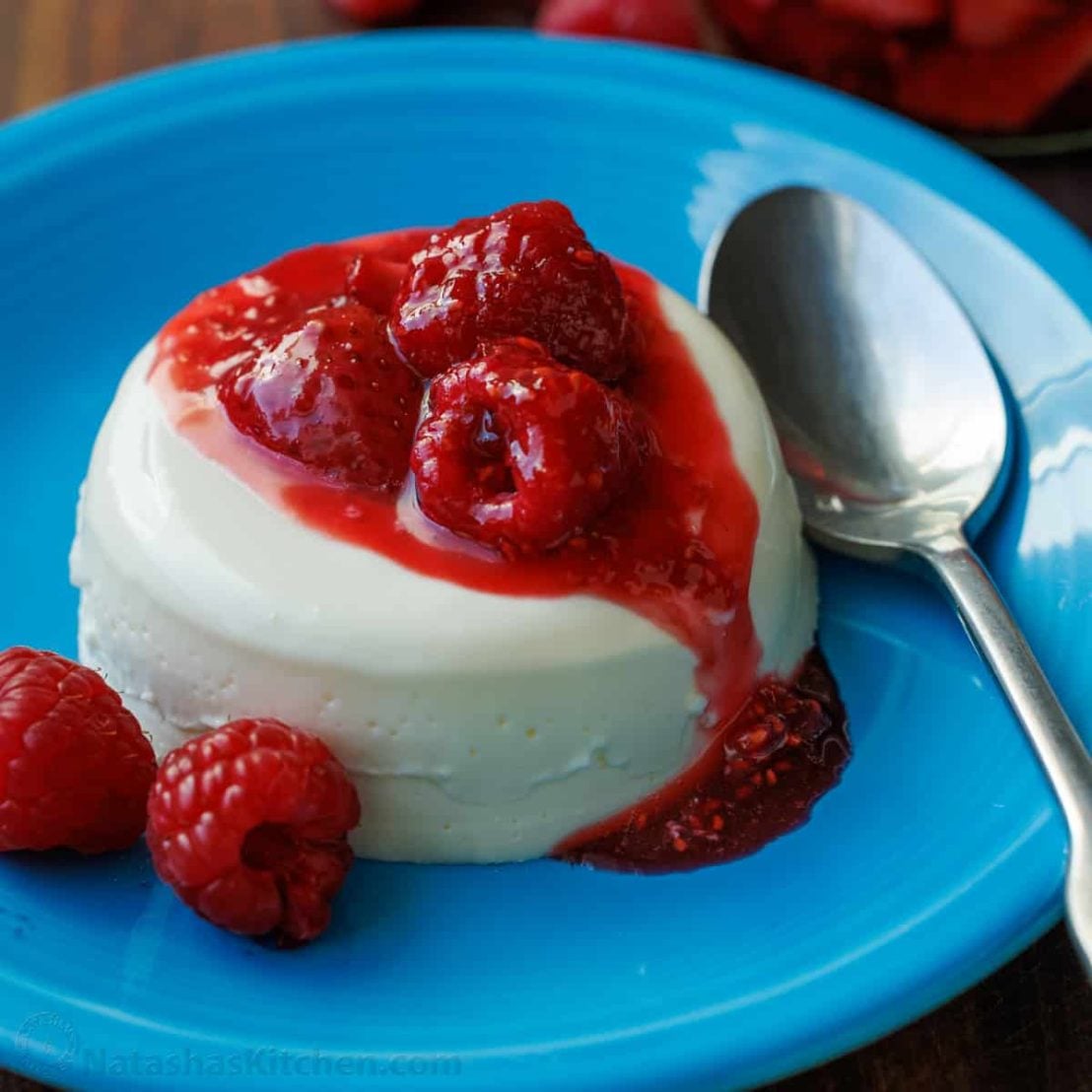 Panna Cotta with berry sauce drizzled over the top, with fresh berries to garnish.