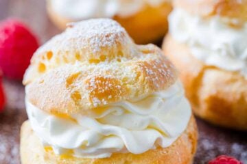 Cream puffs served dusted with powdered sugar surrounded by raspberries