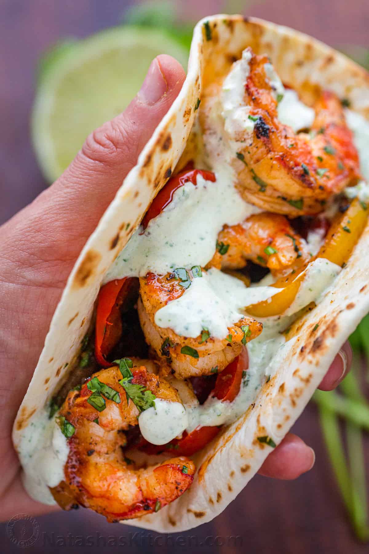 Shrimp Fajitas are an easy, one-pan shrimp recipe an amazing fajita marinade. You'll love this one-pot, 30-minute meal everyone raves about! Hand holding a tortilla with grilled shirmp and ranch sauce