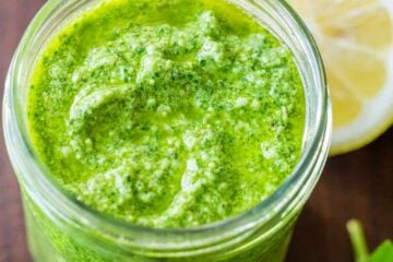 Basil pesto sauce in jar with fresh basil leaves and lemon