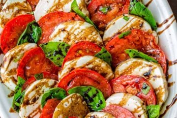 Caprese salad assembled on white platter drizzled with balsamic glaze