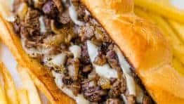 Philly cheesesteak served on hoagie roll with fries and ketchup