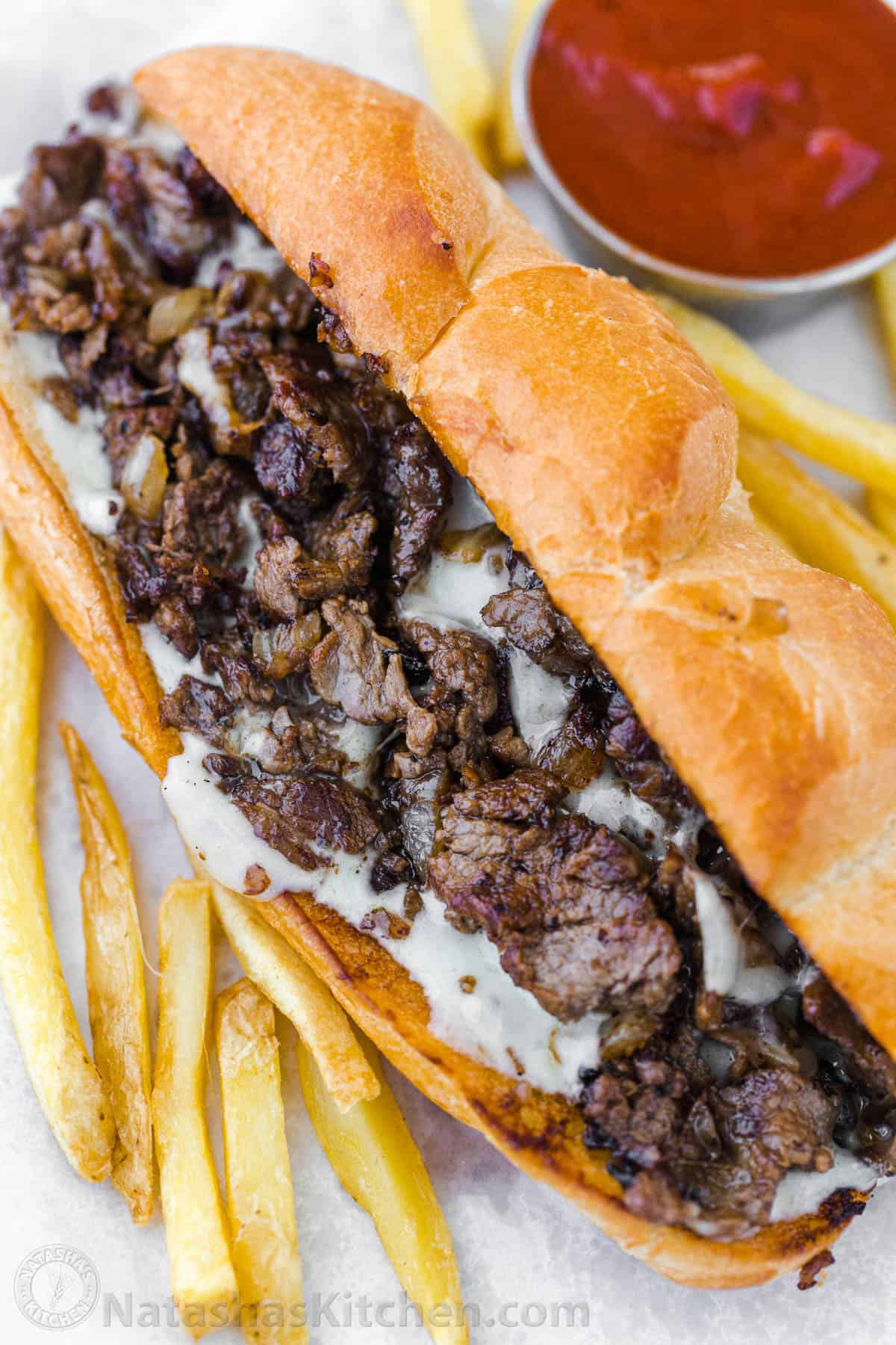 Philly Cheesesteak with tender ribeye steak, melted provolone, and caramelized onion in a garlic butter roll. Easy Philly Cheesesteak Sandwich video how-to. #phillycheesesteak #phillycheesesteakrecipe #phillycheesesteaksandwich #natashaskitchen #cheesesteak #sandwich How to serve Philly cheesesteak sandwiches on a hoagie roll with fries