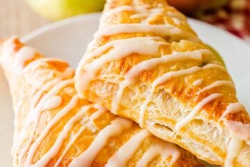 Two apple turnovers on a plate with apples in background