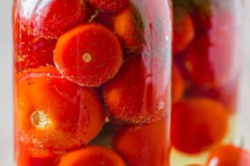 Two jars of canned tomatoes next to fresh tomatoes on the table