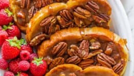 Slices of caramel french toast arranged on a platter with berries scattered