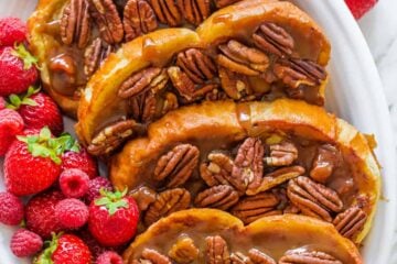 Slices of caramel french toast arranged on a platter with berries scattered