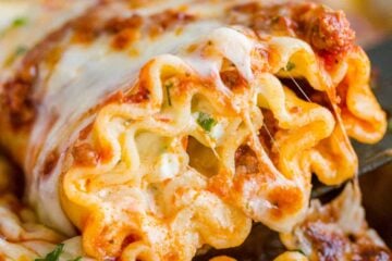Lasagna roll being scooped out of casserole dish with cheese pull
