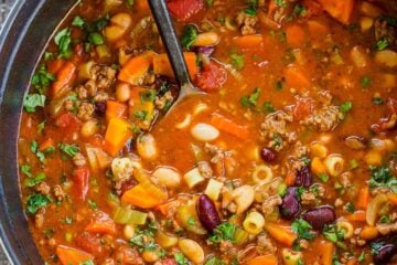 pasta e fagioli in soup pot with serving spoon garnished with basil