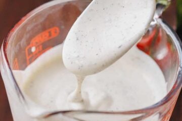 A spoon drizzles ranch dressing into a measuring cup.