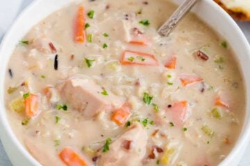 A bowl of chicken and wild rice soup in a bowl with a spoon and slice of bread