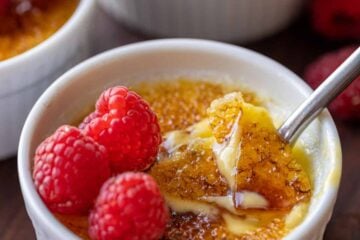 Creme brulee topped with raspberries, with the caramelized sugar topping cracked with a spoon.