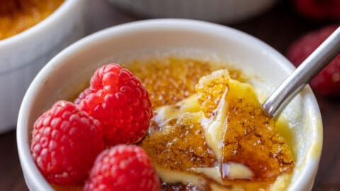 Creme brulee topped with raspberries, with the caramelized sugar topping cracked with a spoon.