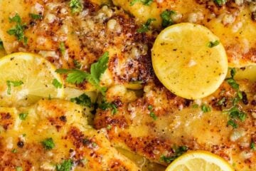Lemon chicken in lemon butter sauce in skillet garnished with lemon slices