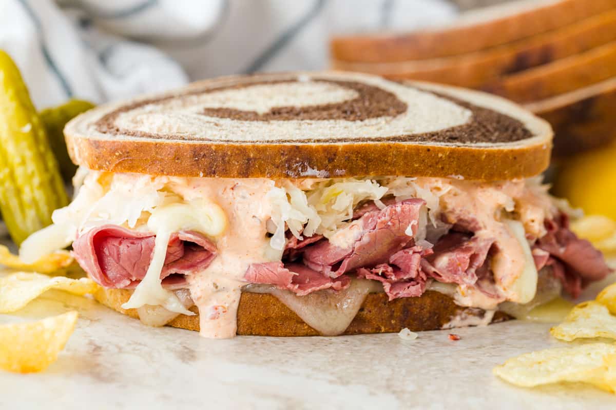 Classic Reuben on a plate with pickles and chips.