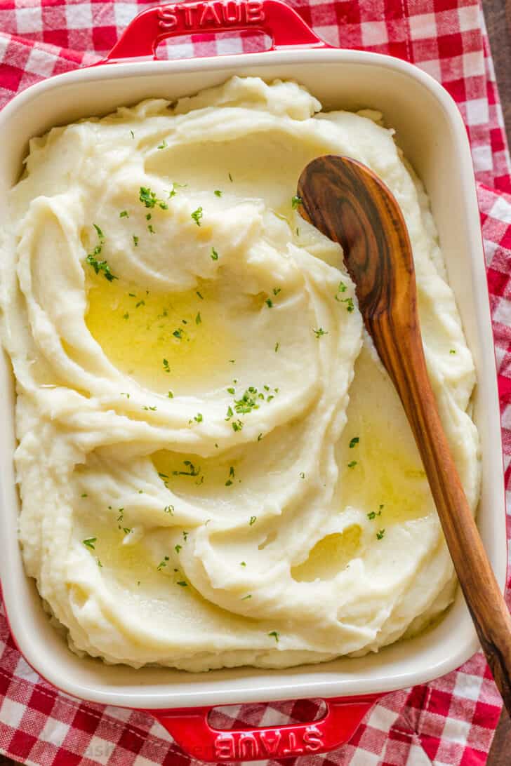 Creamy smooth mashed potatoes in a red casserole dish over a red checkered towel