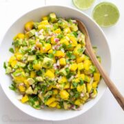 Mango salsa in a white bowl with serving spoon