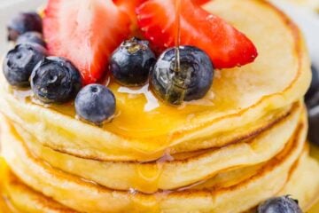 Ricotta Pancakes stacked on plate with fruit and drizzled with maple syrup
