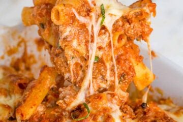 Baked ziti being scooped with a wooden spoon, showing the cheese pulls and layers of noodles, meat, cheese, and sauce.