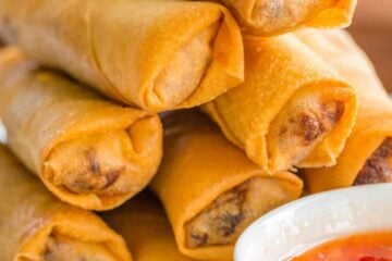 Egg rolls stacked on platter with dipping sauce