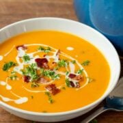 Sweet potato soup in a white bowl garnished with coconut milk