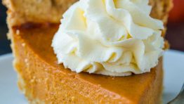 Pumpkin Pie slice topped with whipped cream served on a white plate.