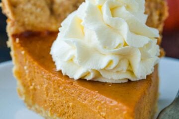 Pumpkin Pie slice topped with whipped cream served on a white plate.