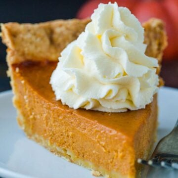 Pumpkin Pie slice topped with whipped cream served on a white plate.