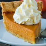 Homemade Pumpkin pie slice on a white plate topped with whipped cream