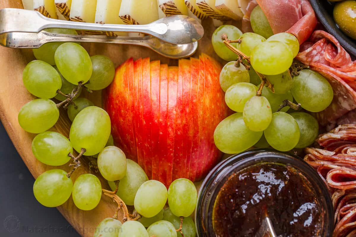 Apple sliced for charcuterie with grape segments around it paired with manchego cheese