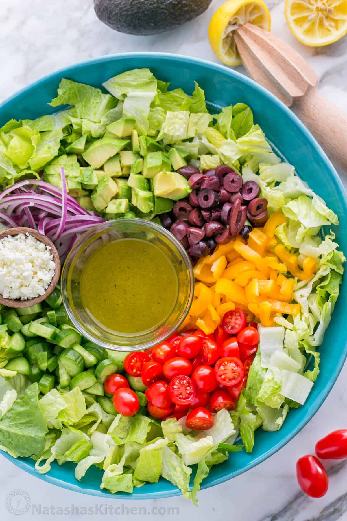 Chopped Greek Salad served in a blue bowl with side of Greek salad dressing ready to drizzle