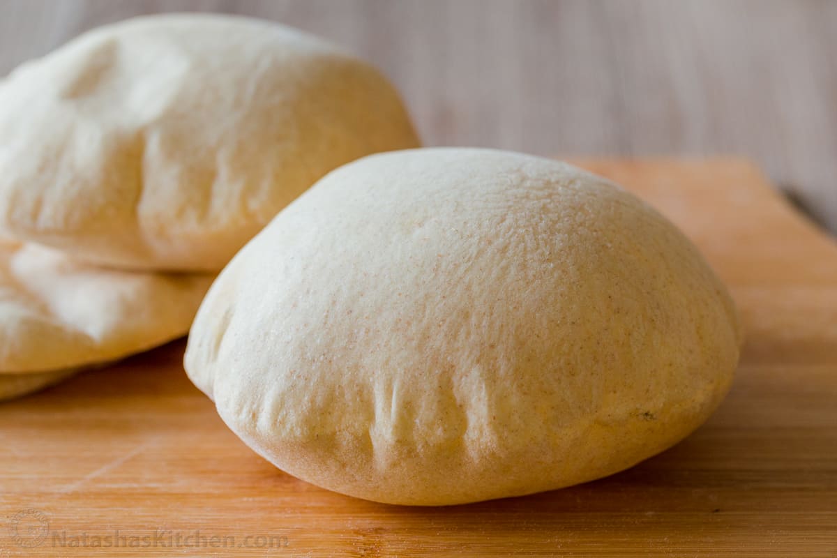 Perfectly puffed pita bread on a countertop with more behind