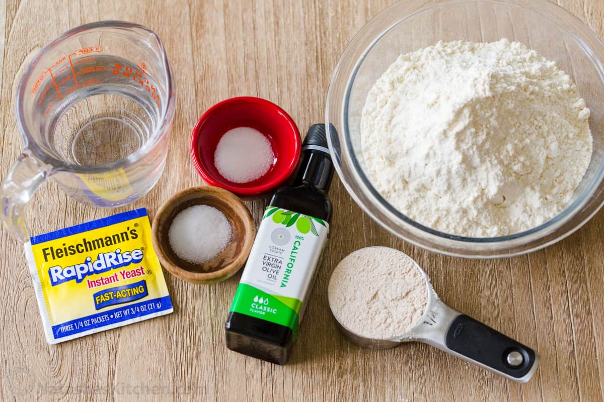 ingredients measured out in bowls for making greek sandwich rounds including water, yeast, sugar, salt, extra virgin olive oil, whole wheat flour and all-purpose flour