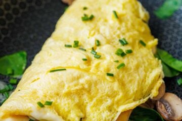 Omelette cooked in a skillet with spinach and mushrooms