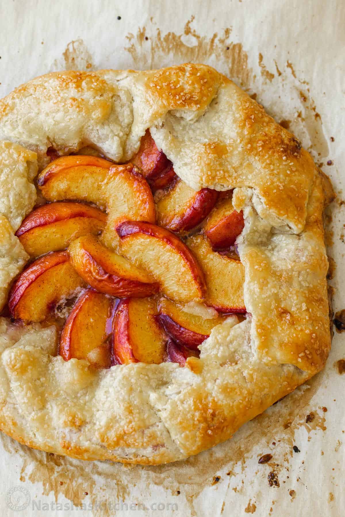 My easy peach galette recipe features fresh peaches on top of a flaky, rustic crust. It has all the flavor of peach pie without as much fuss. Overhead view of whole peach galette baked on parchment paper