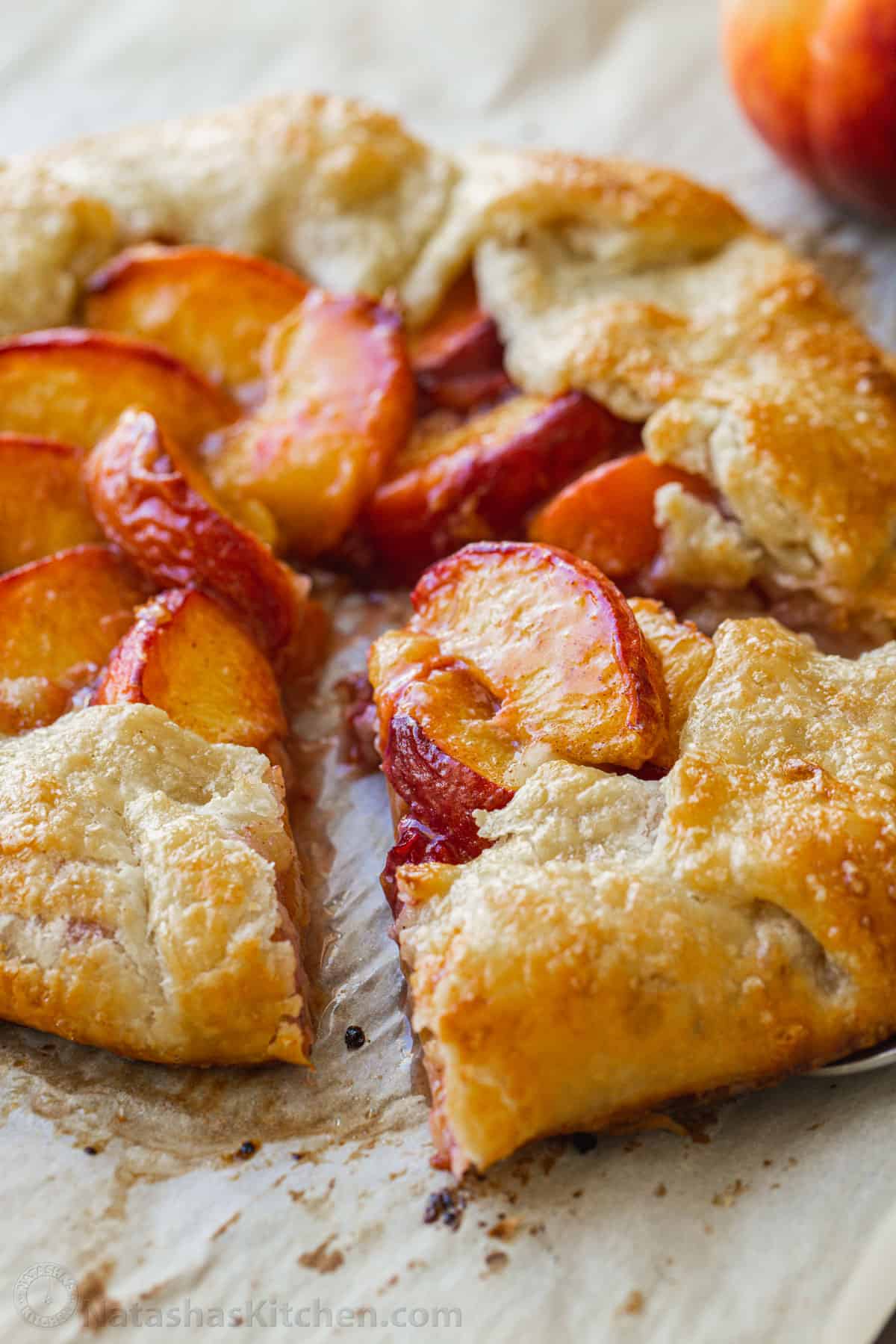 My easy peach galette recipe features fresh peaches on top of a flaky, rustic crust. It has all the flavor of peach pie without as much fuss. Piece of peach galette being removed