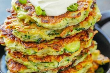 Stack of zucchini fritters topped with sour cream and scallions