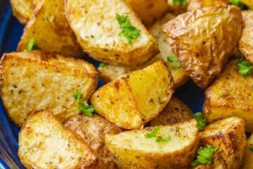 Close up of air fryer roasted potatoes on a blue platter, garnished with parsley.